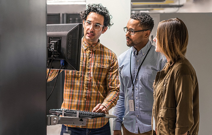 A group of people standing in a room looking at at computer monitor